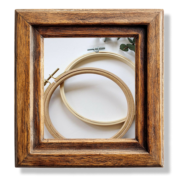 Two embroidery hoops sitting on a white table in a wooden frame.