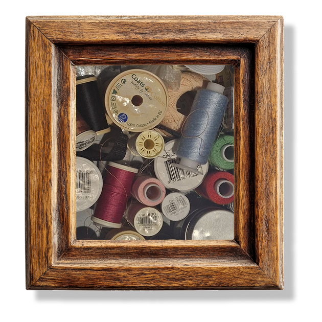 A close up of different spools of thread in a wooden frame.