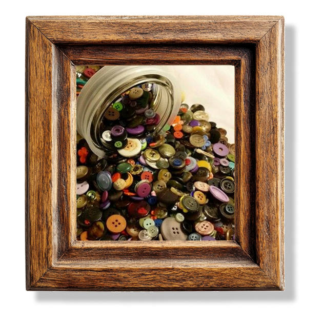 A tipped over jar of buttons in a wooden frame.