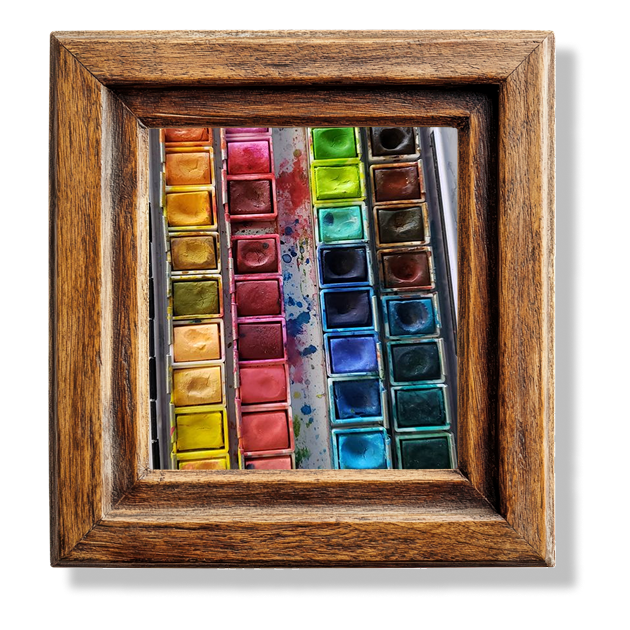 A close up of a used water color palette in a wooden frame.